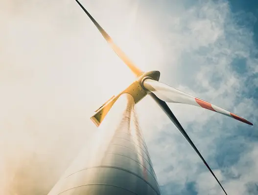 White and red wind turbine tower and blades taken from the base of the tower with cloudy blue sky in background